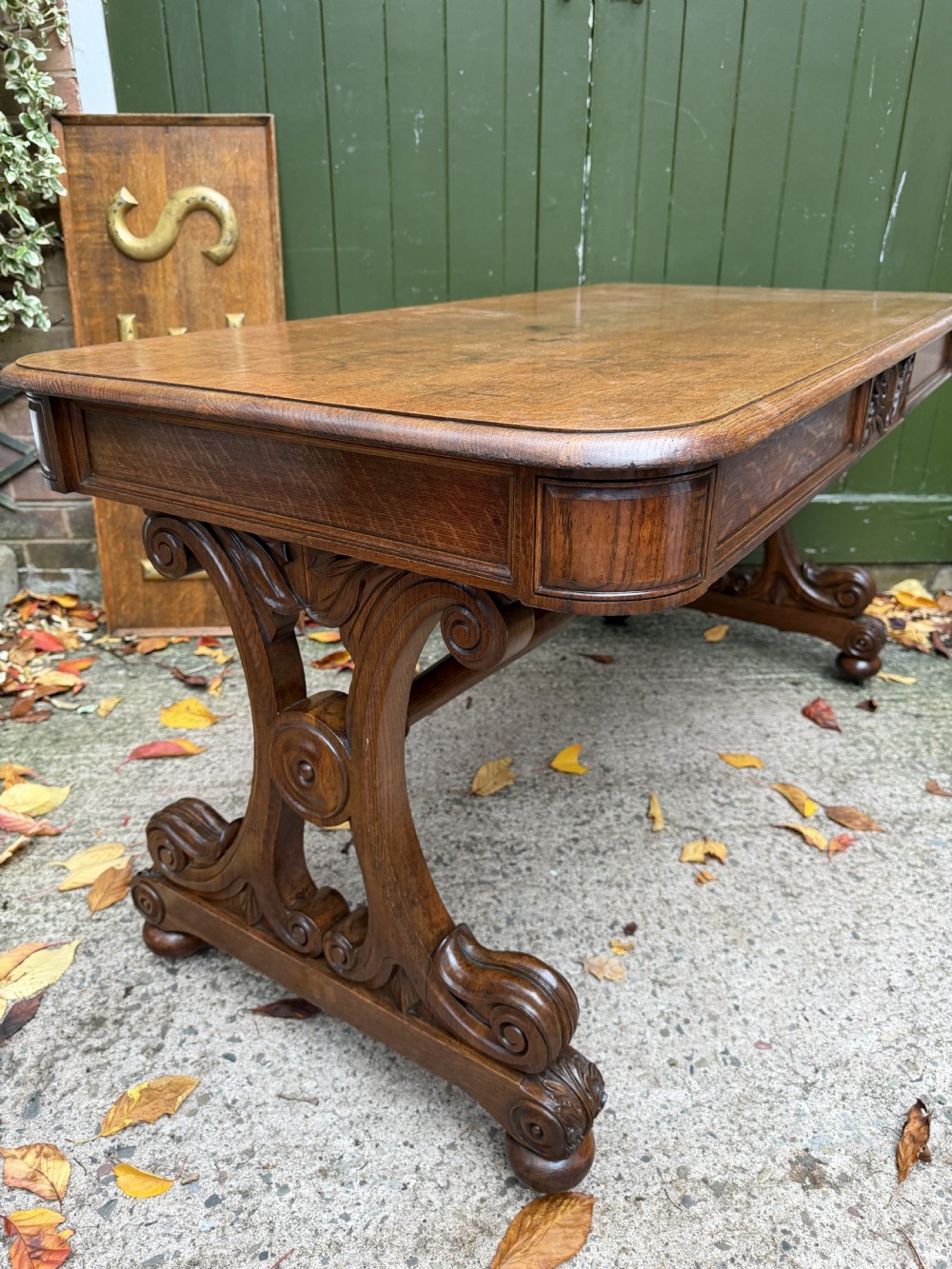 An early 19th-century William IV oak library table featuring a central carved acorn frieze panel, scrolled trestle supports, and a turned stretcher base. View III