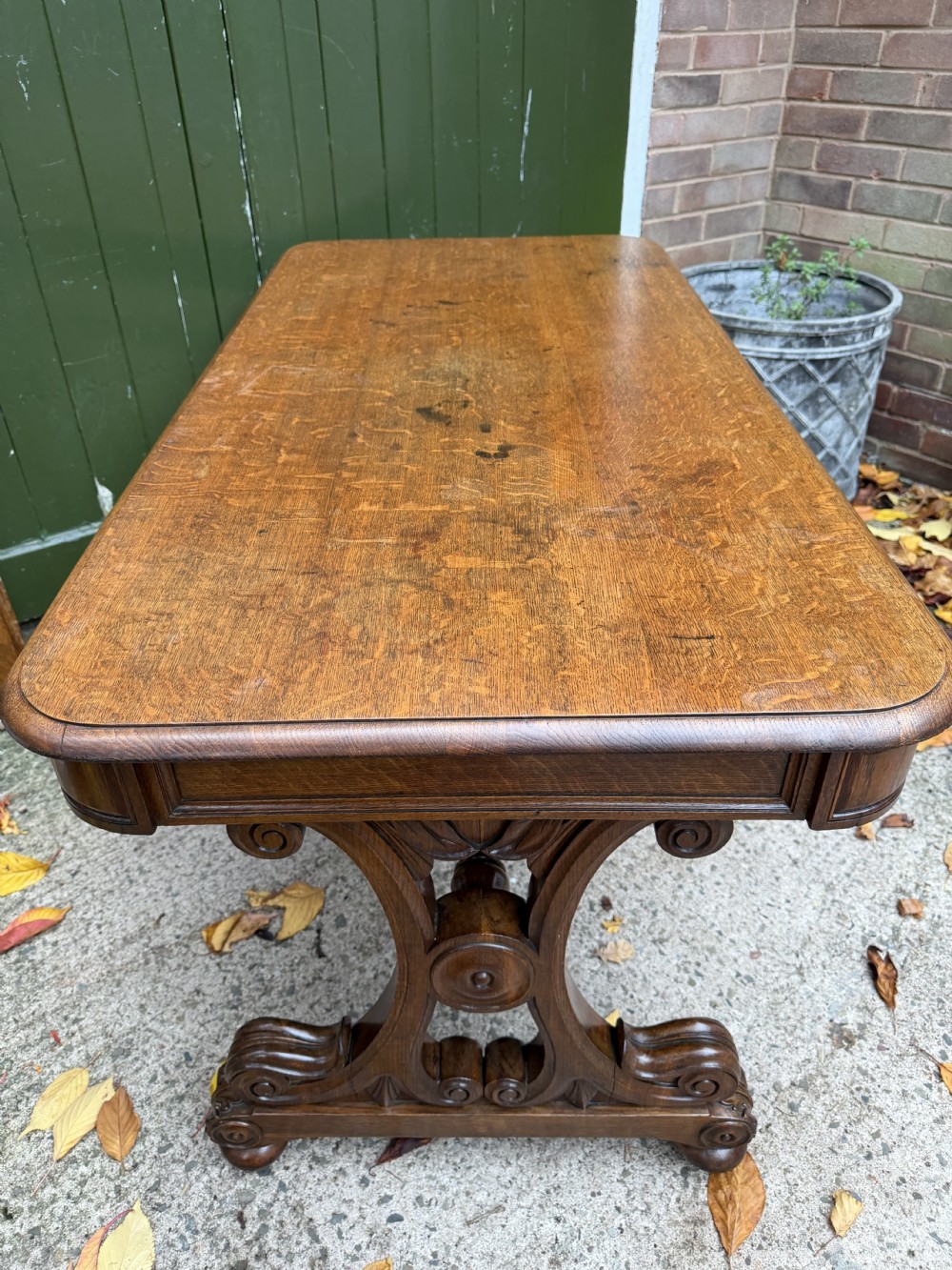 An early 19th-century William IV oak library table featuring a central carved acorn frieze panel, scrolled trestle supports, and a turned stretcher base. View VI