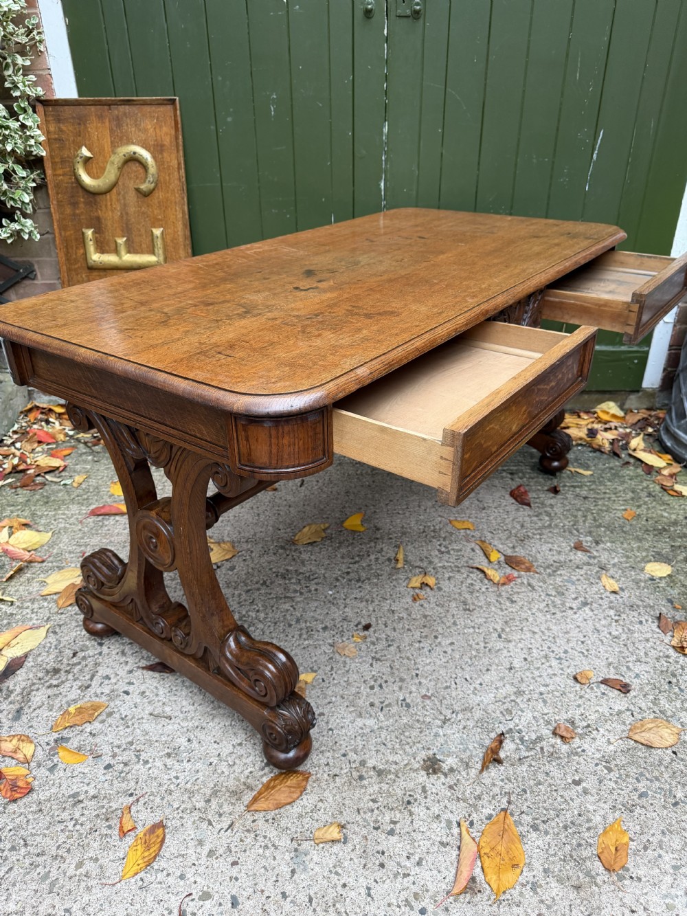 An early 19th-century William IV oak library table featuring a central carved acorn frieze panel, scrolled trestle supports, and a turned stretcher base. View VII