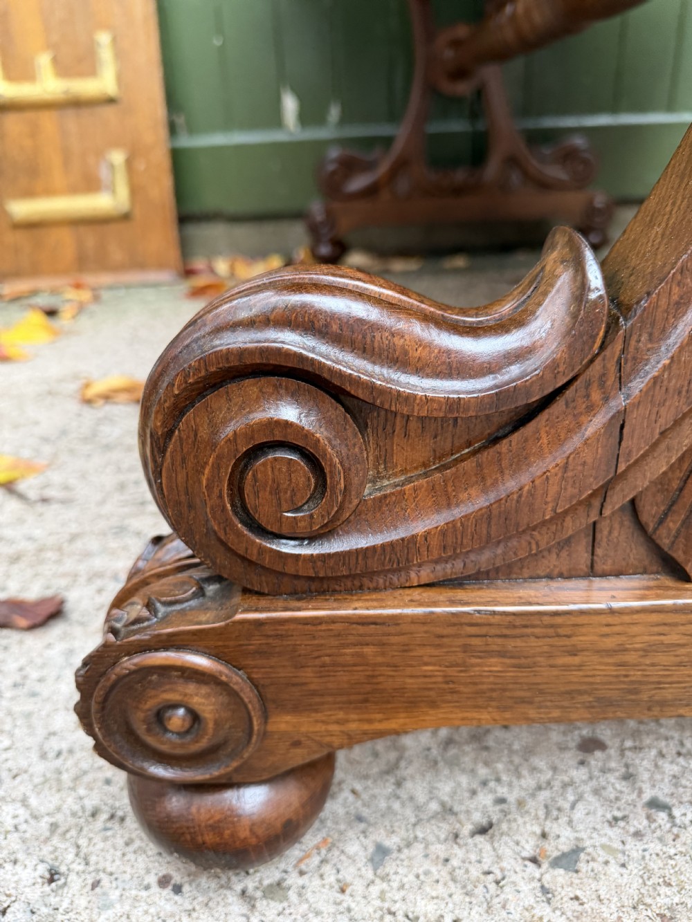 An early 19th-century William IV oak library table featuring a central carved acorn frieze panel, scrolled trestle supports, and a turned stretcher base. View IX