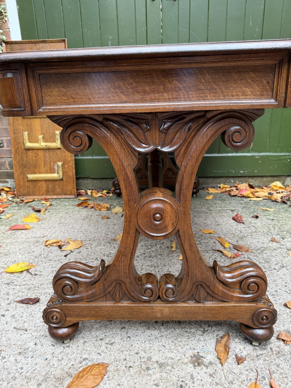 An early 19th-century William IV oak library table featuring a central carved acorn frieze panel, scrolled trestle supports, and a turned stretcher base. View XI