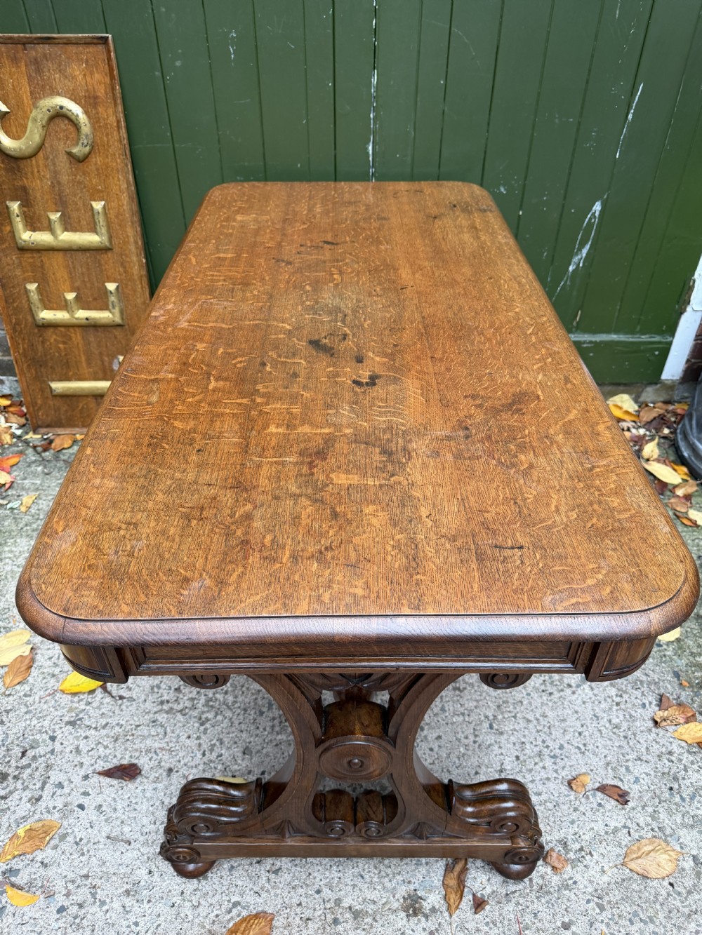 An early 19th-century William IV oak library table featuring a central carved acorn frieze panel, scrolled trestle supports, and a turned stretcher base. View XIII
