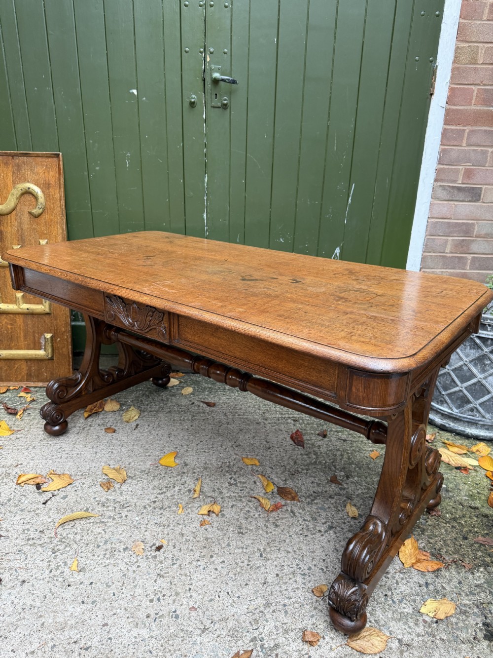 An early 19th-century William IV oak library table featuring a central carved acorn frieze panel, scrolled trestle supports, and a turned stretcher base. View XIV