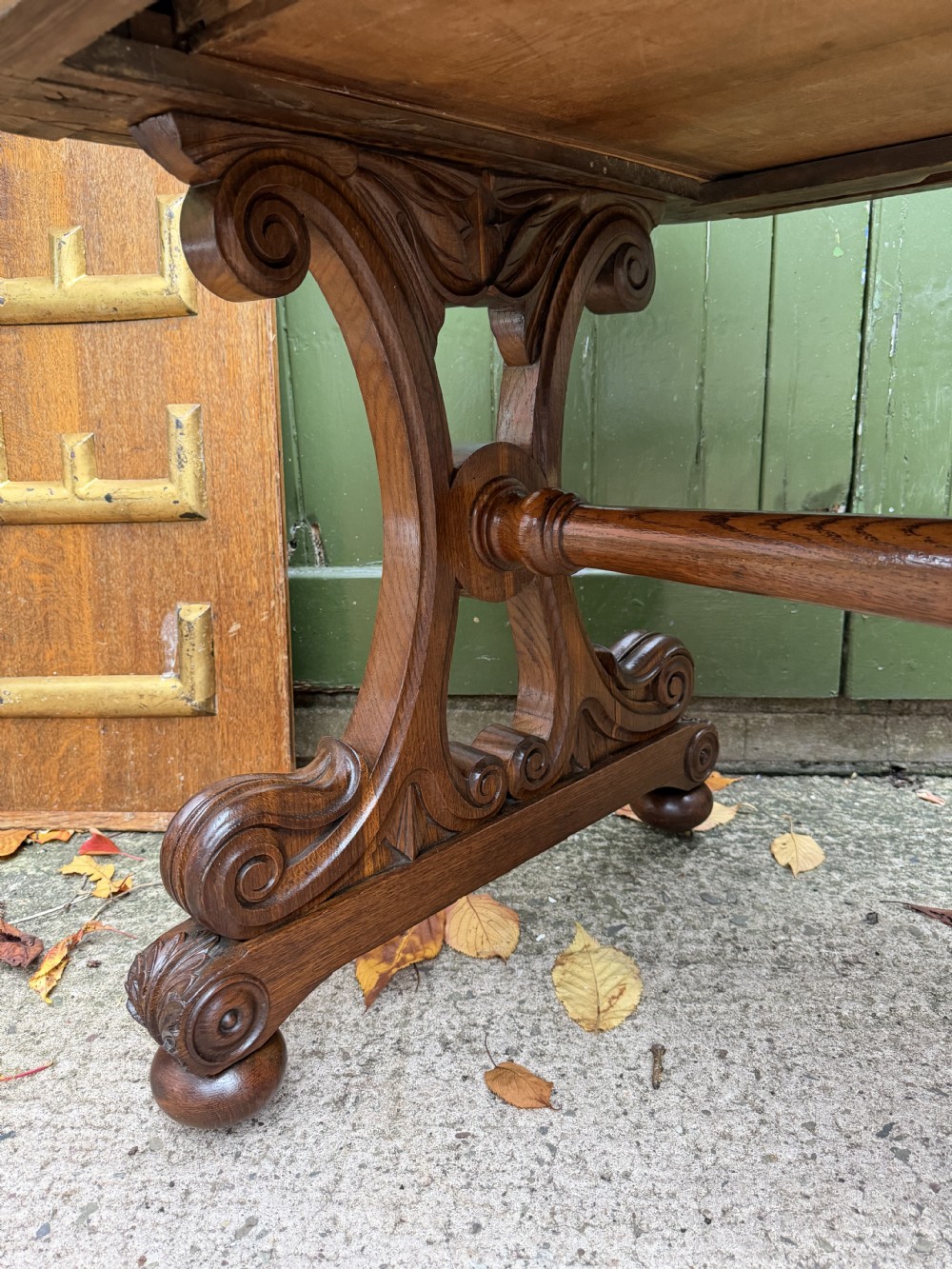 An early 19th-century William IV oak library table featuring a central carved acorn frieze panel, scrolled trestle supports, and a turned stretcher base. View XVIII