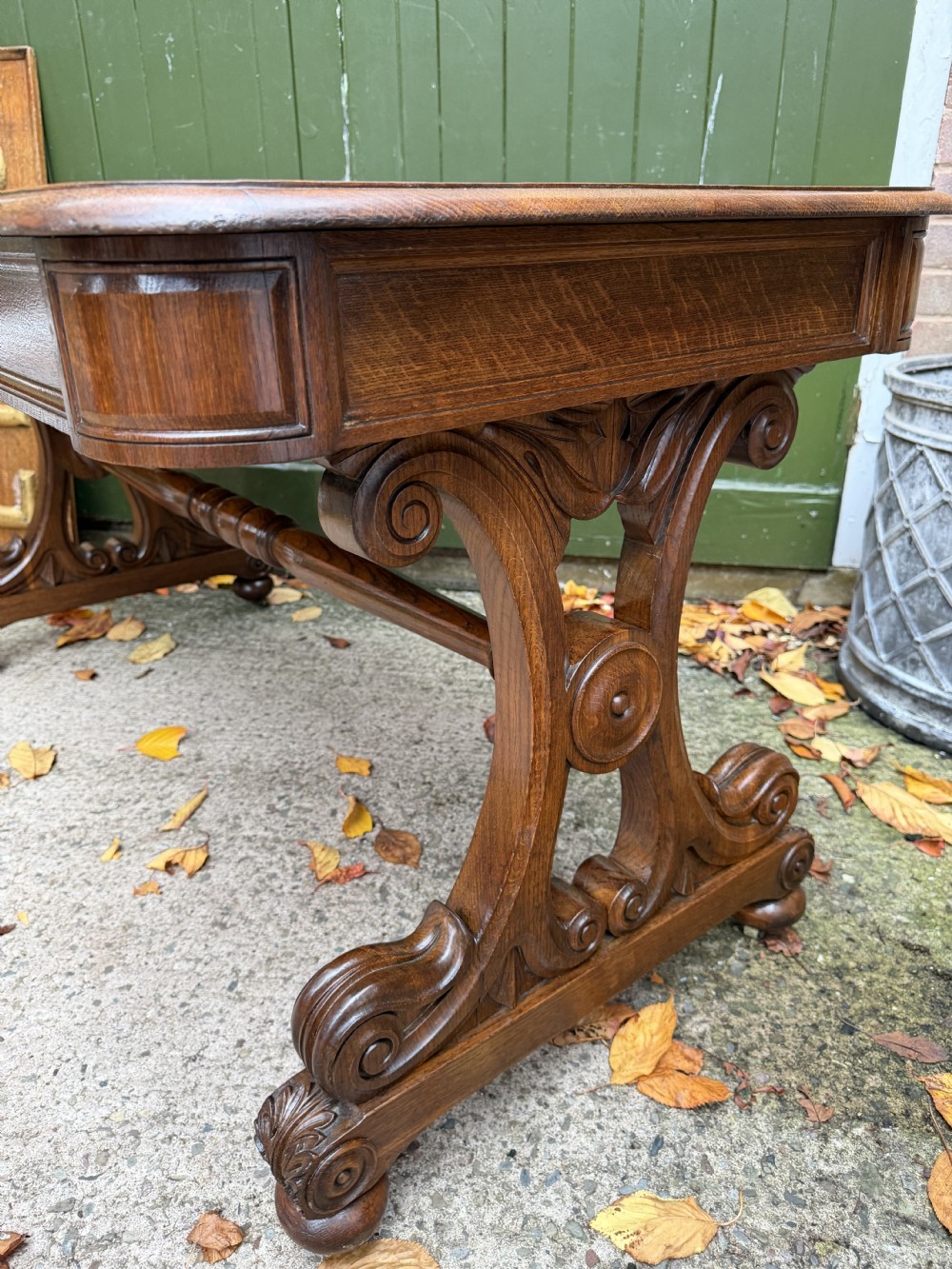An early 19th-century William IV oak library table featuring a central carved acorn frieze panel, scrolled trestle supports, and a turned stretcher base. View XIX