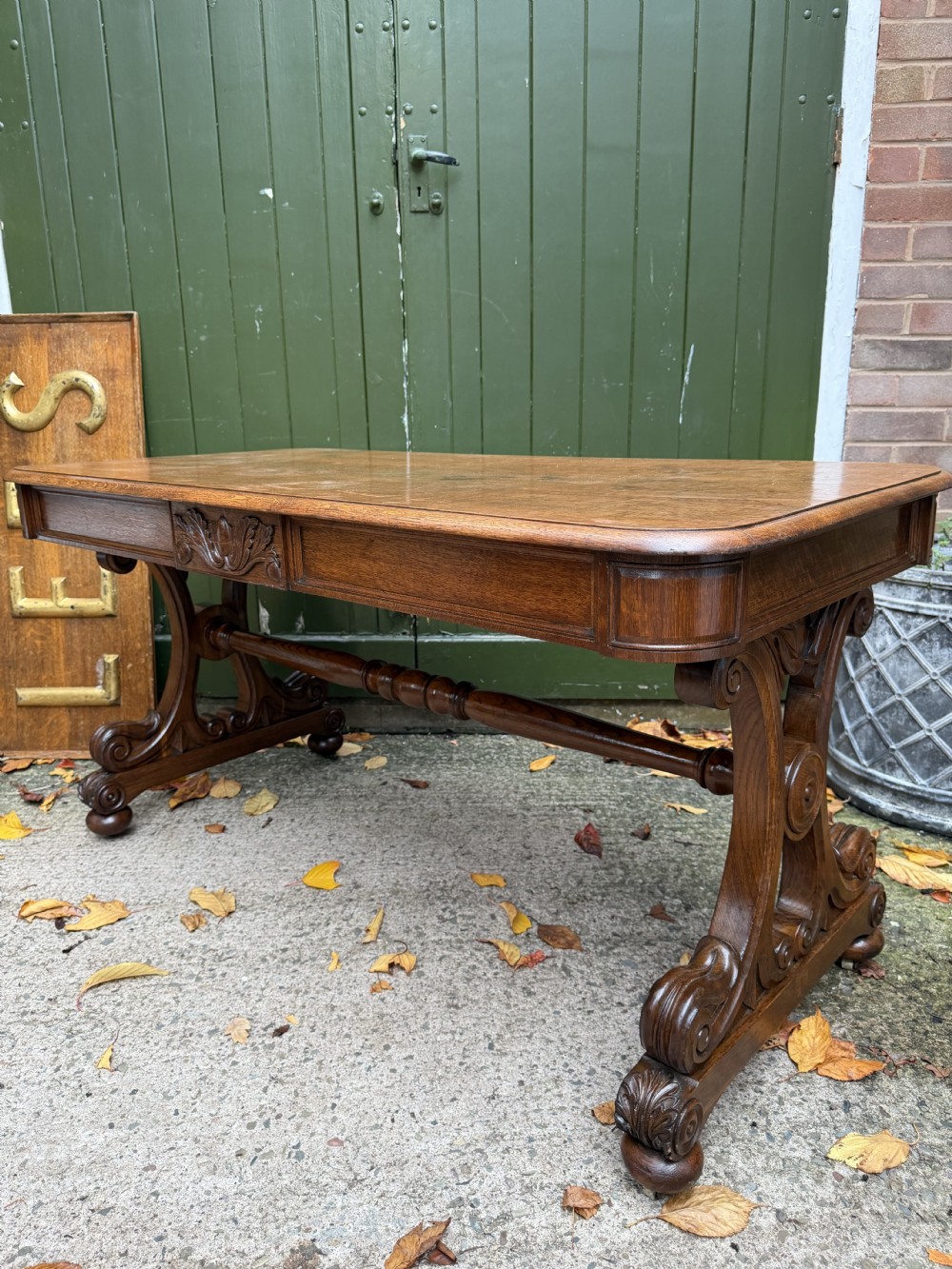 An early 19th-century William IV oak library table featuring a central carved acorn frieze panel, scrolled trestle supports, and a turned stretcher base. View XXI