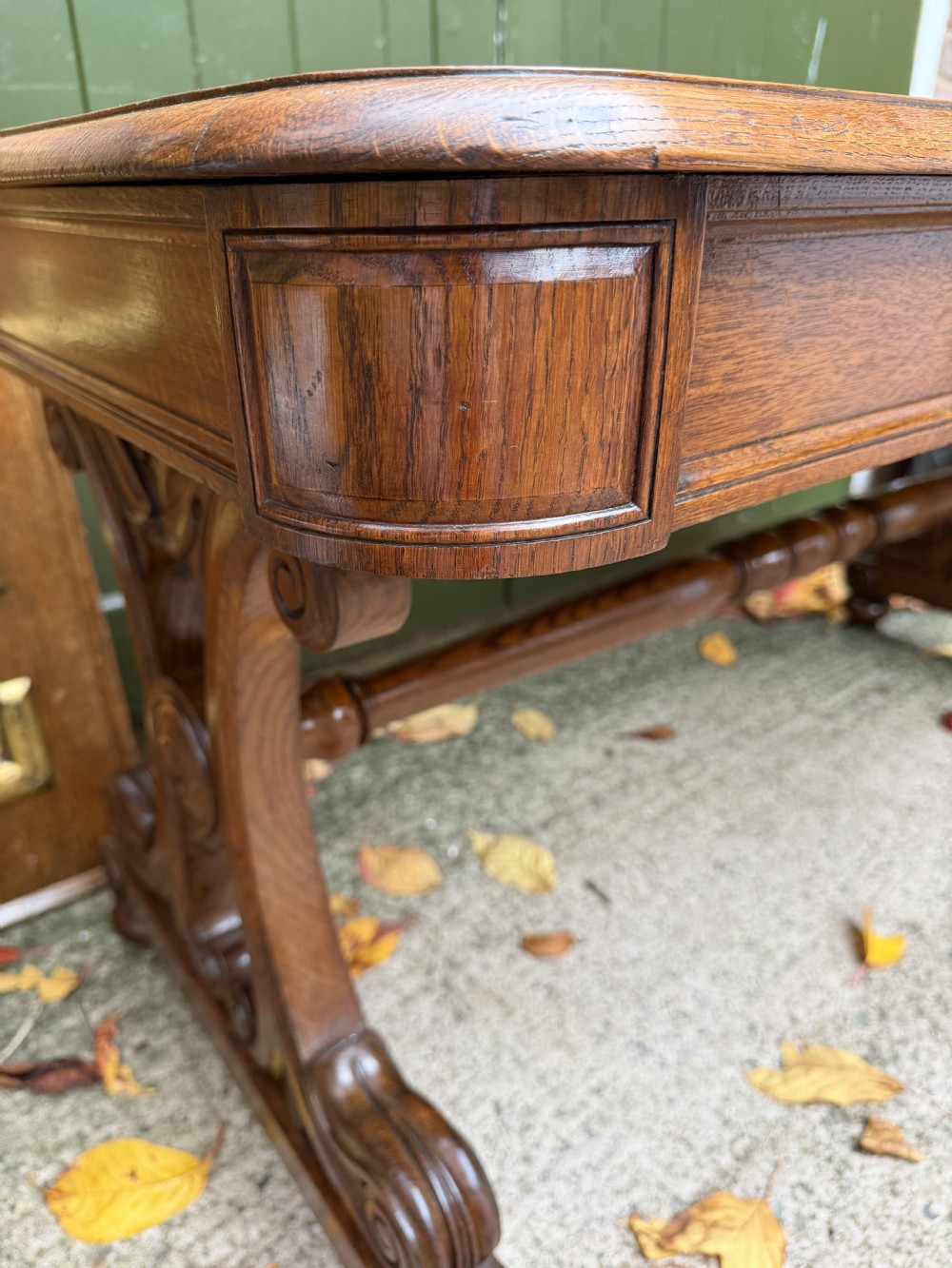An early 19th-century William IV oak library table featuring a central carved acorn frieze panel, scrolled trestle supports, and a turned stretcher base. View XXIV