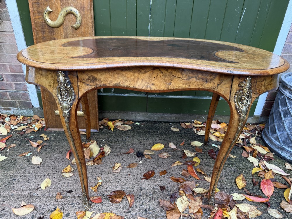 A mid-19th-century kidney-shaped burr walnut writing table with an inset leather surface and cast ormolu mounts on cabriole legs.