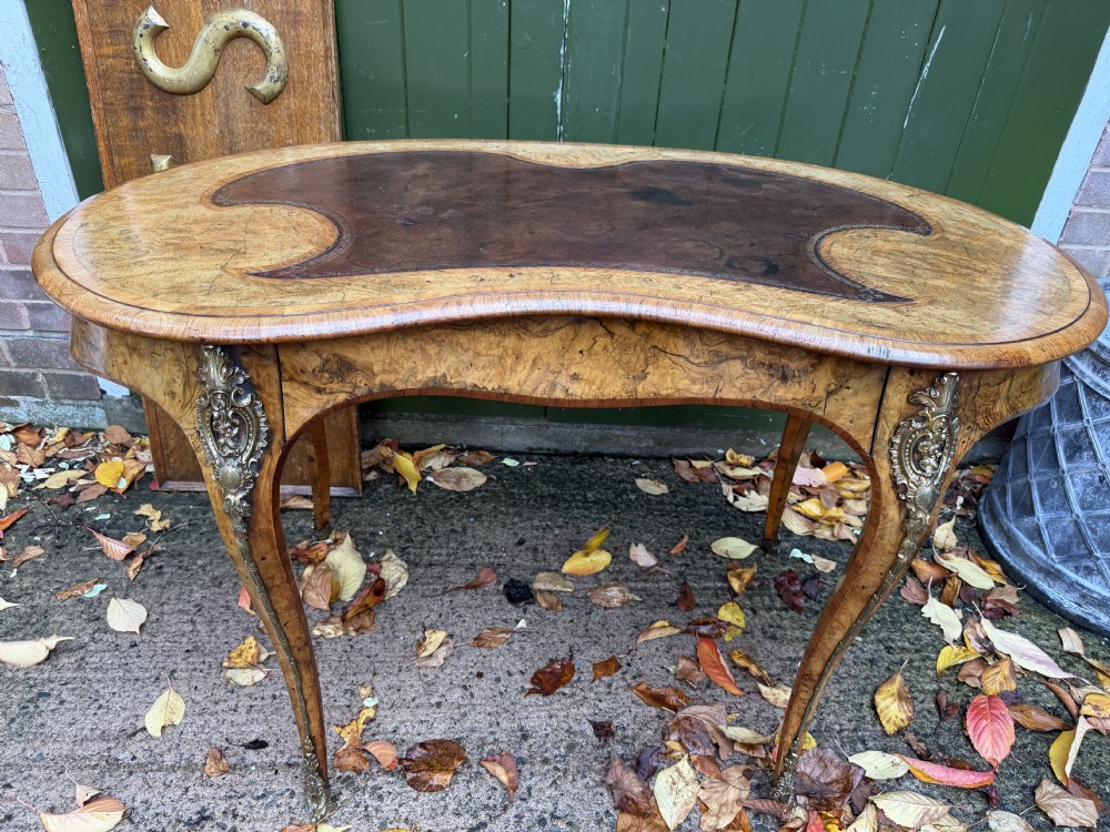 A mid-19th-century kidney-shaped burr walnut writing table with an inset leather surface and cast ormolu mounts on cabriole legs. View II