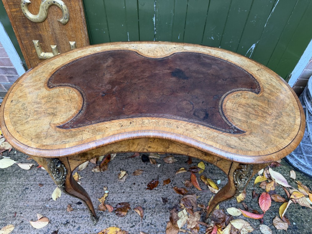 A mid-19th-century kidney-shaped burr walnut writing table with an inset leather surface and cast ormolu mounts on cabriole legs. View VI