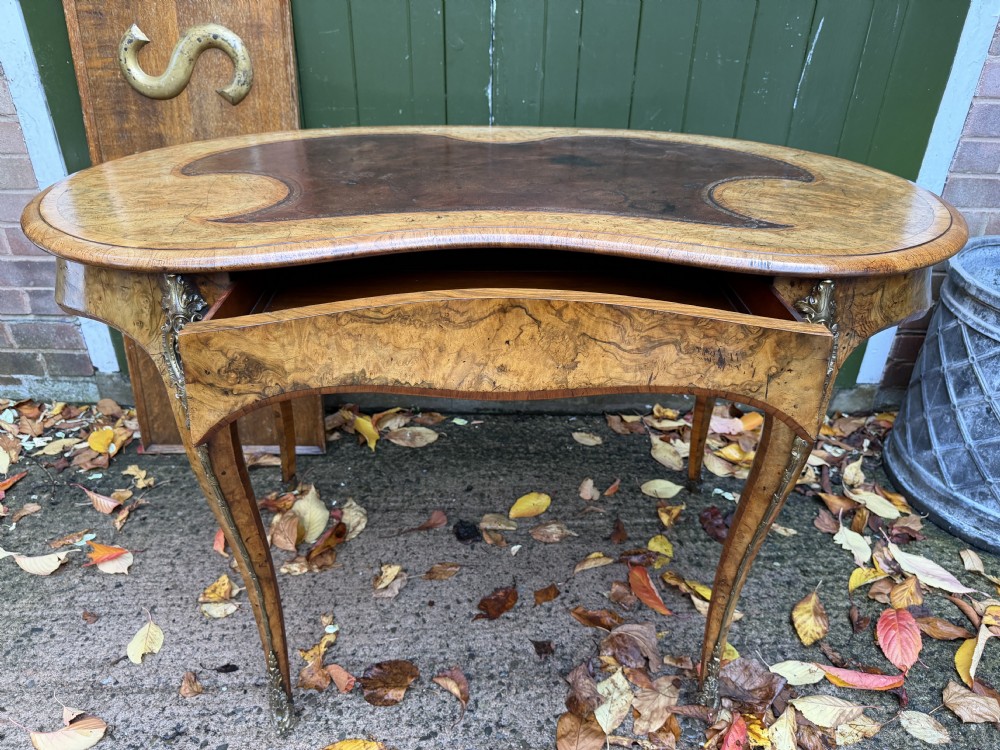 A mid-19th-century kidney-shaped burr walnut writing table with an inset leather surface and cast ormolu mounts on cabriole legs. View IX