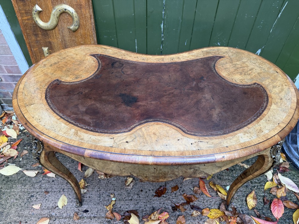 A mid-19th-century kidney-shaped burr walnut writing table with an inset leather surface and cast ormolu mounts on cabriole legs. View XX