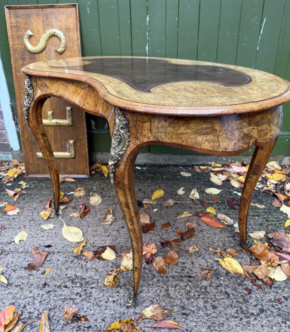 A mid-19th-century kidney-shaped burr walnut writing table with an inset leather surface and cast ormolu mounts on cabriole legs. View XXIV