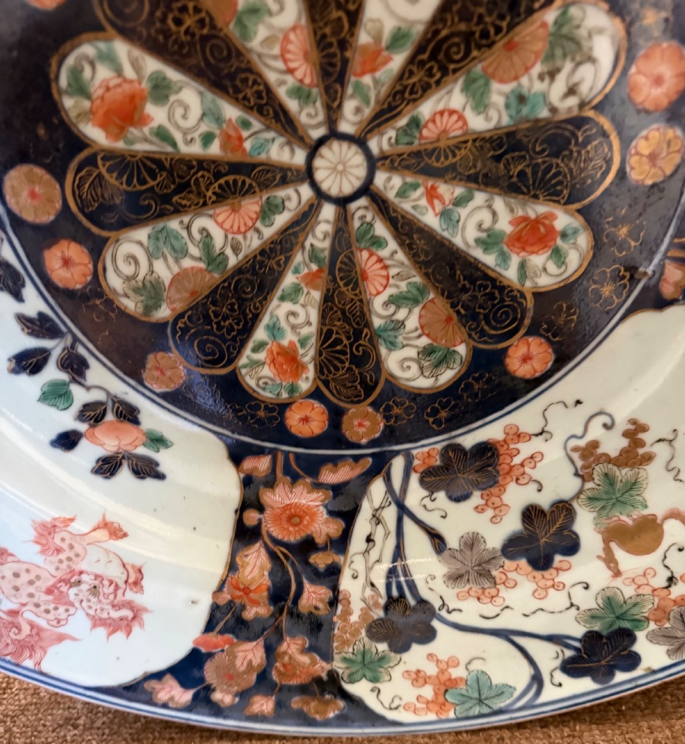 A circular Japanese Imari porcelain dished charger decorated in cobalt blue, iron-red, green, and gold with central chrysanthemum and floral panel designs. View VIII