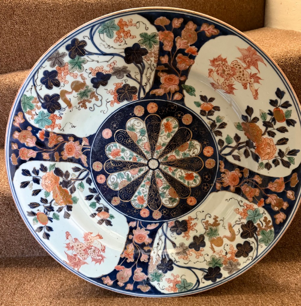 A circular Japanese Imari porcelain dished charger decorated in cobalt blue, iron-red, green, and gold with central chrysanthemum and floral panel designs. View IX