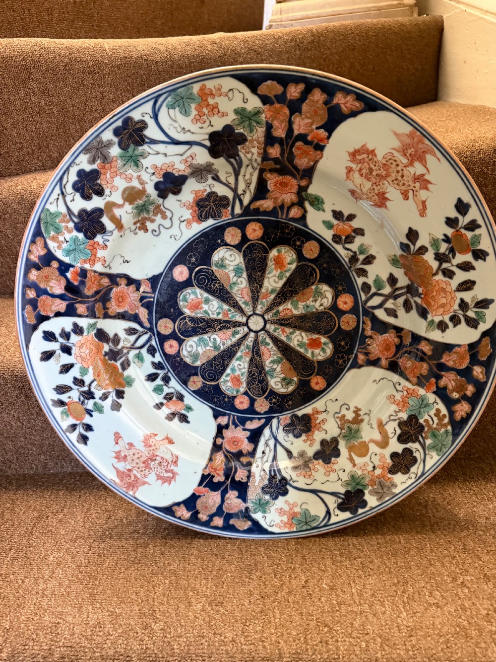 A circular Japanese Imari porcelain dished charger decorated in cobalt blue, iron-red, green, and gold with central chrysanthemum and floral panel designs. View X