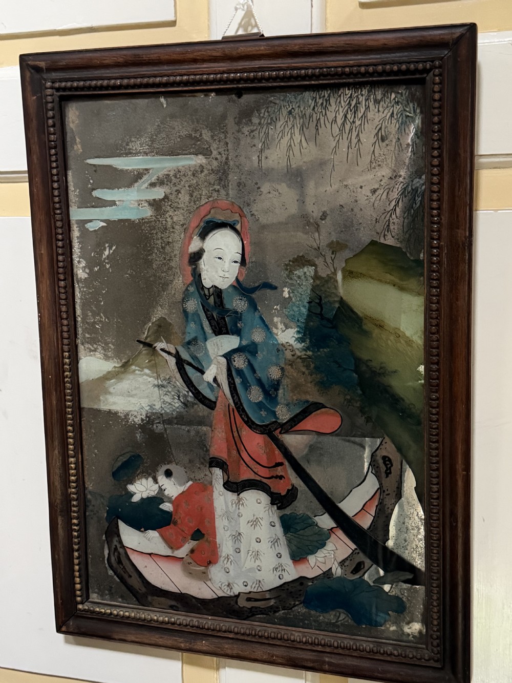An early nineteenth-century Chinese export reverse glass picture featuring a figure on a boat against a silvered mirror background, encased in a dark wooden frame with beaded inner moulding. View X