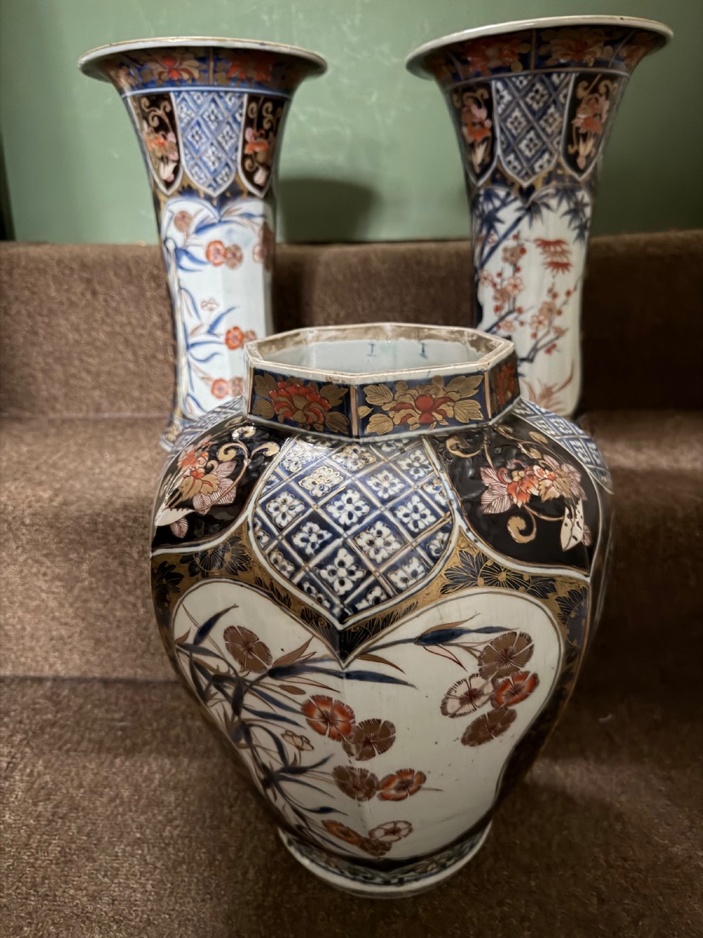 A three-piece Japanese Imari porcelain garniture featuring a central octagonal baluster jar flanked by two trumpet-shaped beaker vases, decorated with floral panels in cobalt blue, iron red, and gold. View II