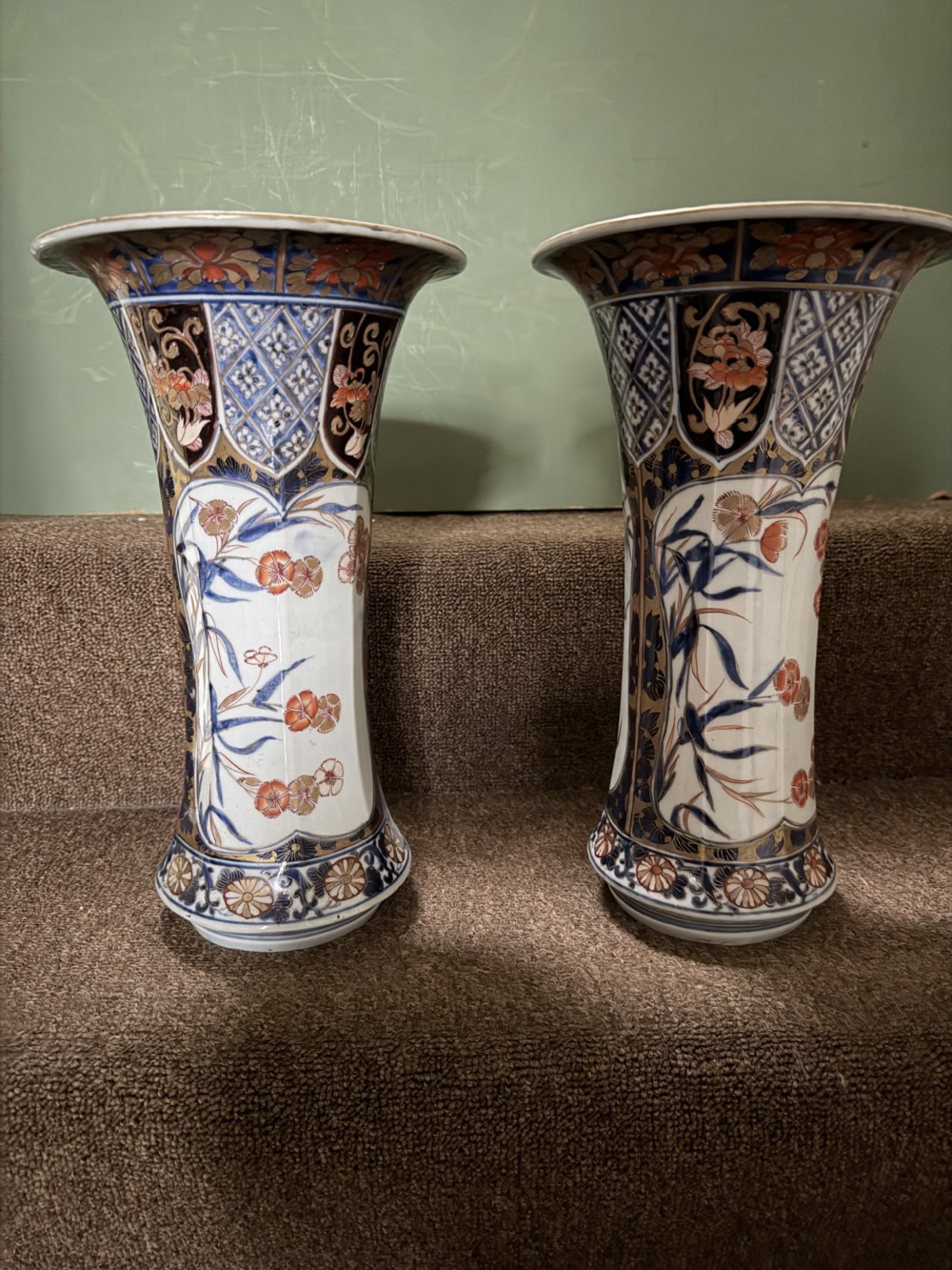 A three-piece Japanese Imari porcelain garniture featuring a central octagonal baluster jar flanked by two trumpet-shaped beaker vases, decorated with floral panels in cobalt blue, iron red, and gold. View VI