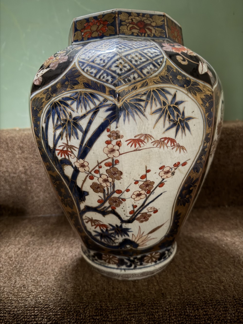 A three-piece Japanese Imari porcelain garniture featuring a central octagonal baluster jar flanked by two trumpet-shaped beaker vases, decorated with floral panels in cobalt blue, iron red, and gold. View IX