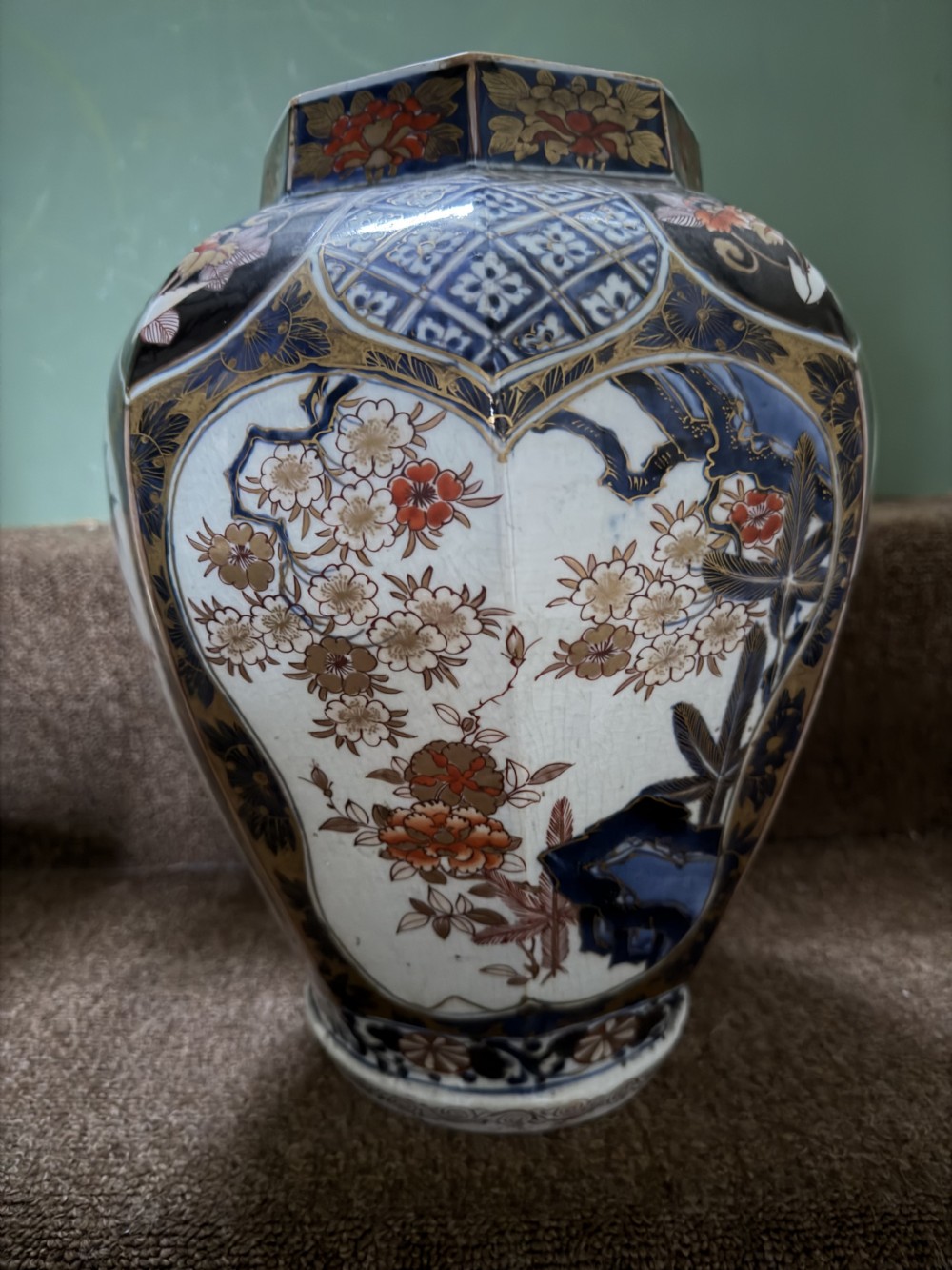 A three-piece Japanese Imari porcelain garniture featuring a central octagonal baluster jar flanked by two trumpet-shaped beaker vases, decorated with floral panels in cobalt blue, iron red, and gold. View X