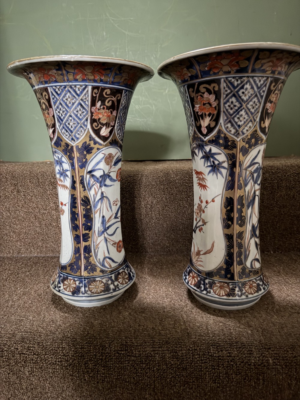 A three-piece Japanese Imari porcelain garniture featuring a central octagonal baluster jar flanked by two trumpet-shaped beaker vases, decorated with floral panels in cobalt blue, iron red, and gold. View XIX