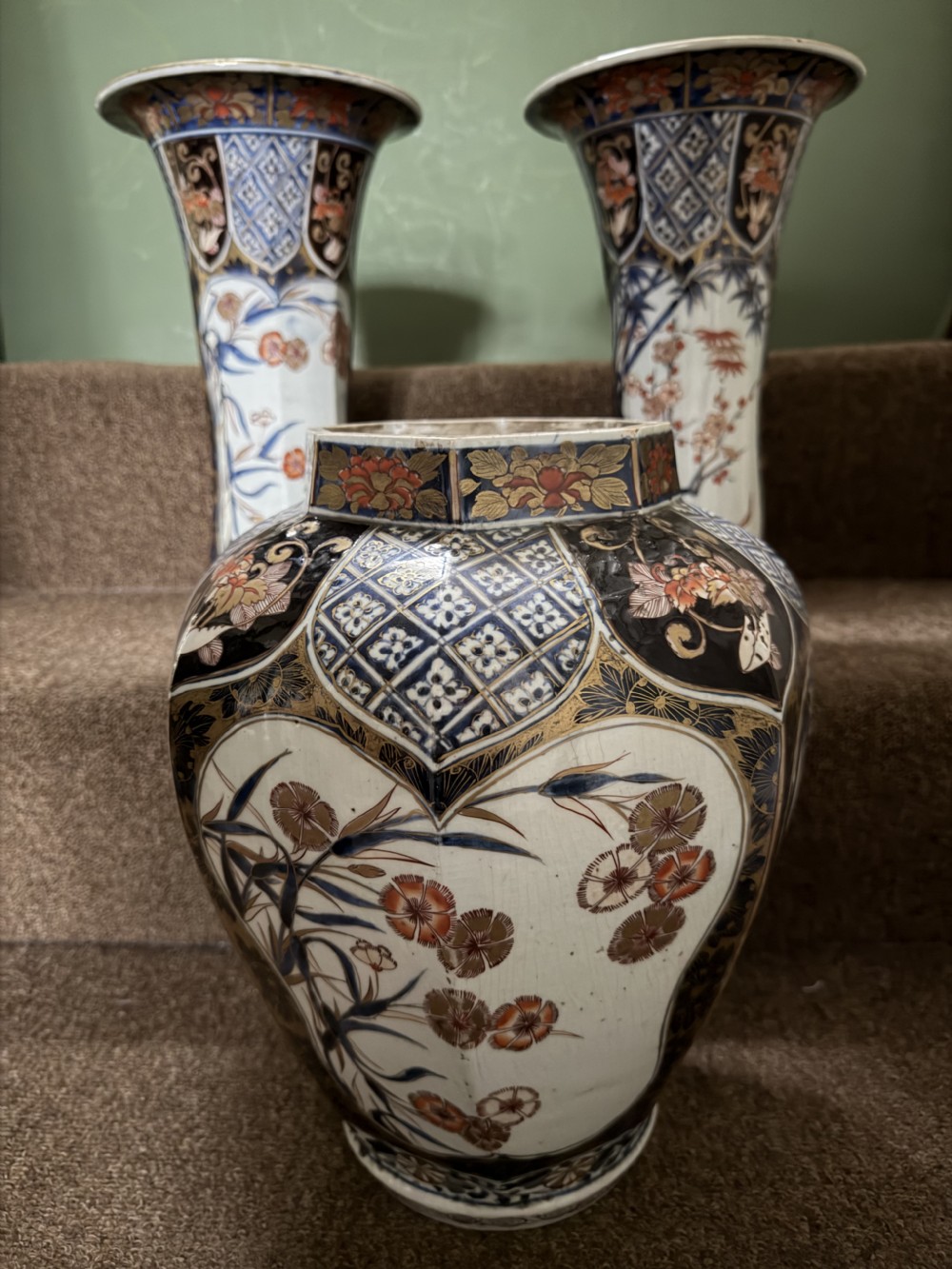 A three-piece Japanese Imari porcelain garniture featuring a central octagonal baluster jar flanked by two trumpet-shaped beaker vases, decorated with floral panels in cobalt blue, iron red, and gold. View XX