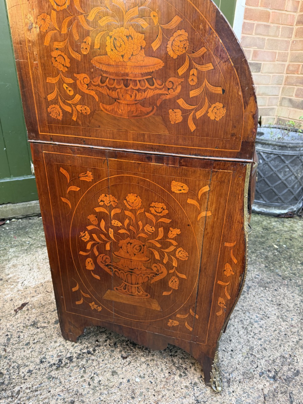 An antique Dutch walnut bureau with floral marquetry inlays, a curved cylinder front, three drawers, and decorative brass handles. View V