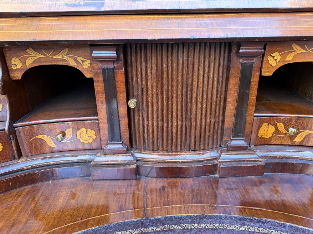 An antique Dutch walnut bureau with floral marquetry inlays, a curved cylinder front, three drawers, and decorative brass handles. View X