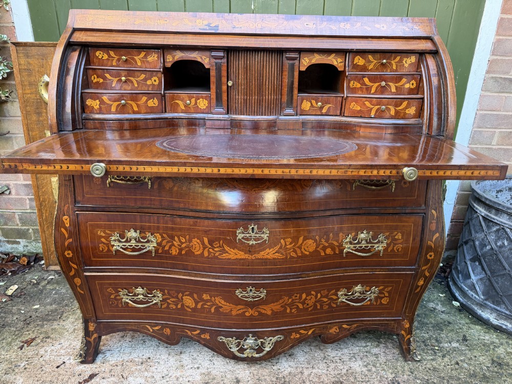 An antique Dutch walnut bureau with floral marquetry inlays, a curved cylinder front, three drawers, and decorative brass handles. View XI