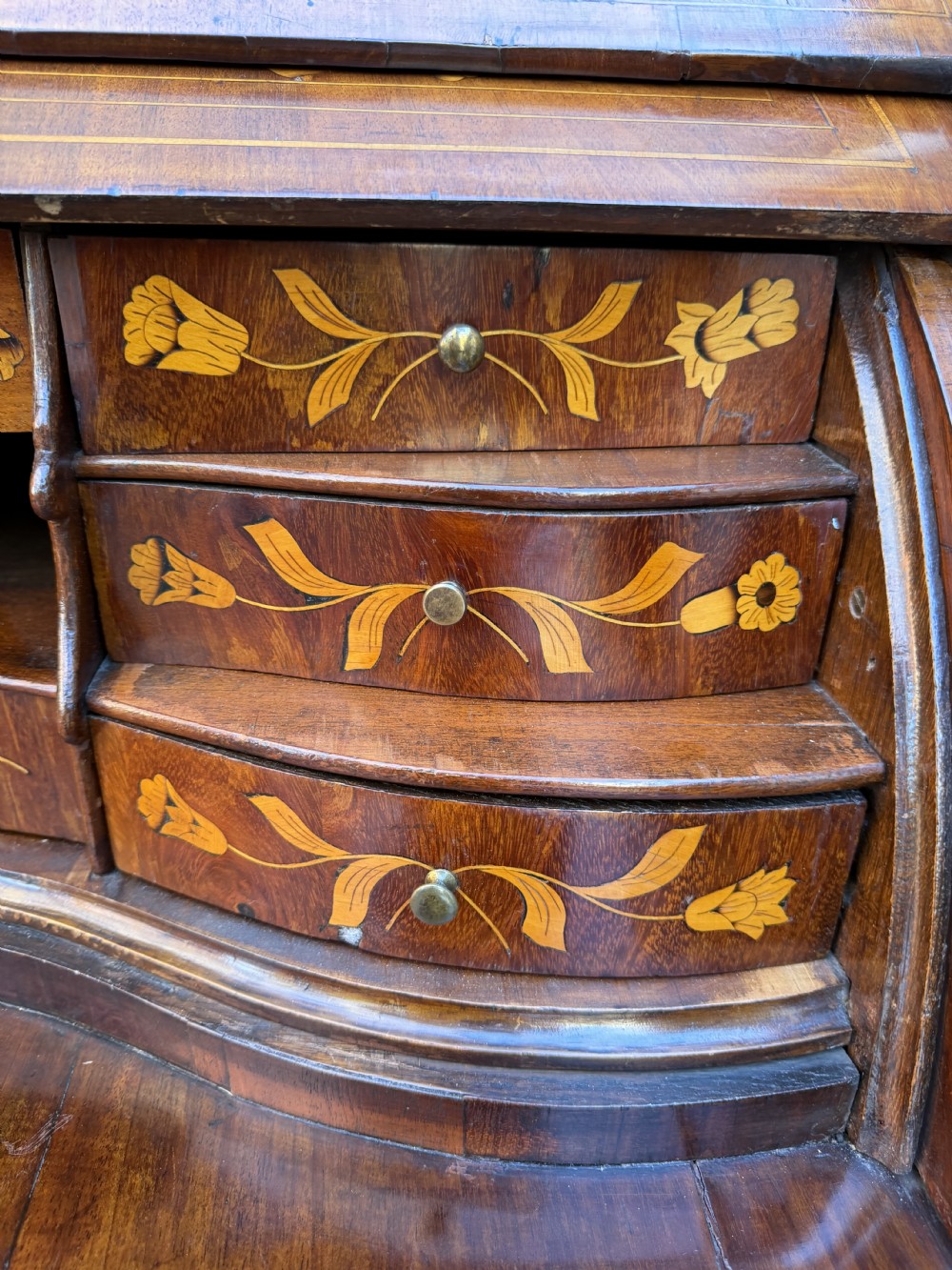 An antique Dutch walnut bureau with floral marquetry inlays, a curved cylinder front, three drawers, and decorative brass handles. View XV