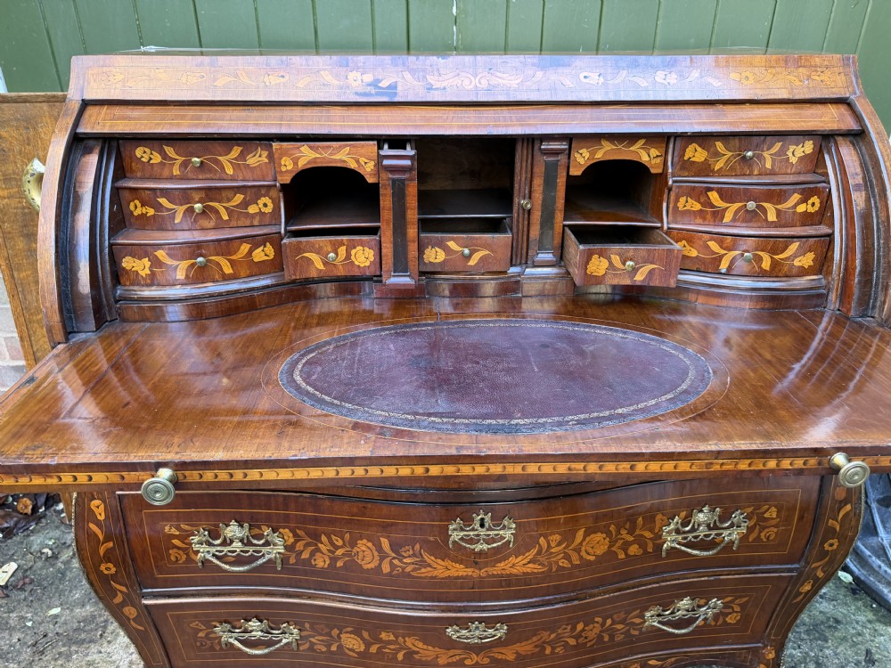 An antique Dutch walnut bureau with floral marquetry inlays, a curved cylinder front, three drawers, and decorative brass handles. View XVI
