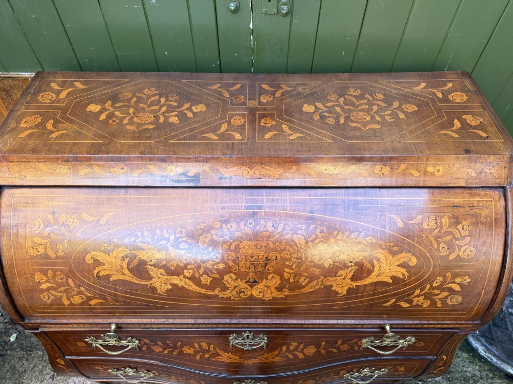 An antique Dutch walnut bureau with floral marquetry inlays, a curved cylinder front, three drawers, and decorative brass handles. View XVIII