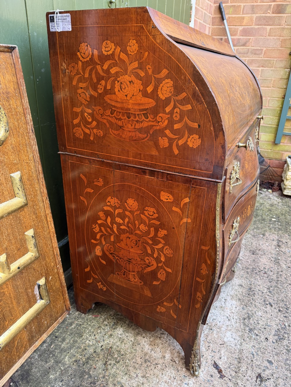 An antique Dutch walnut bureau with floral marquetry inlays, a curved cylinder front, three drawers, and decorative brass handles. View XX