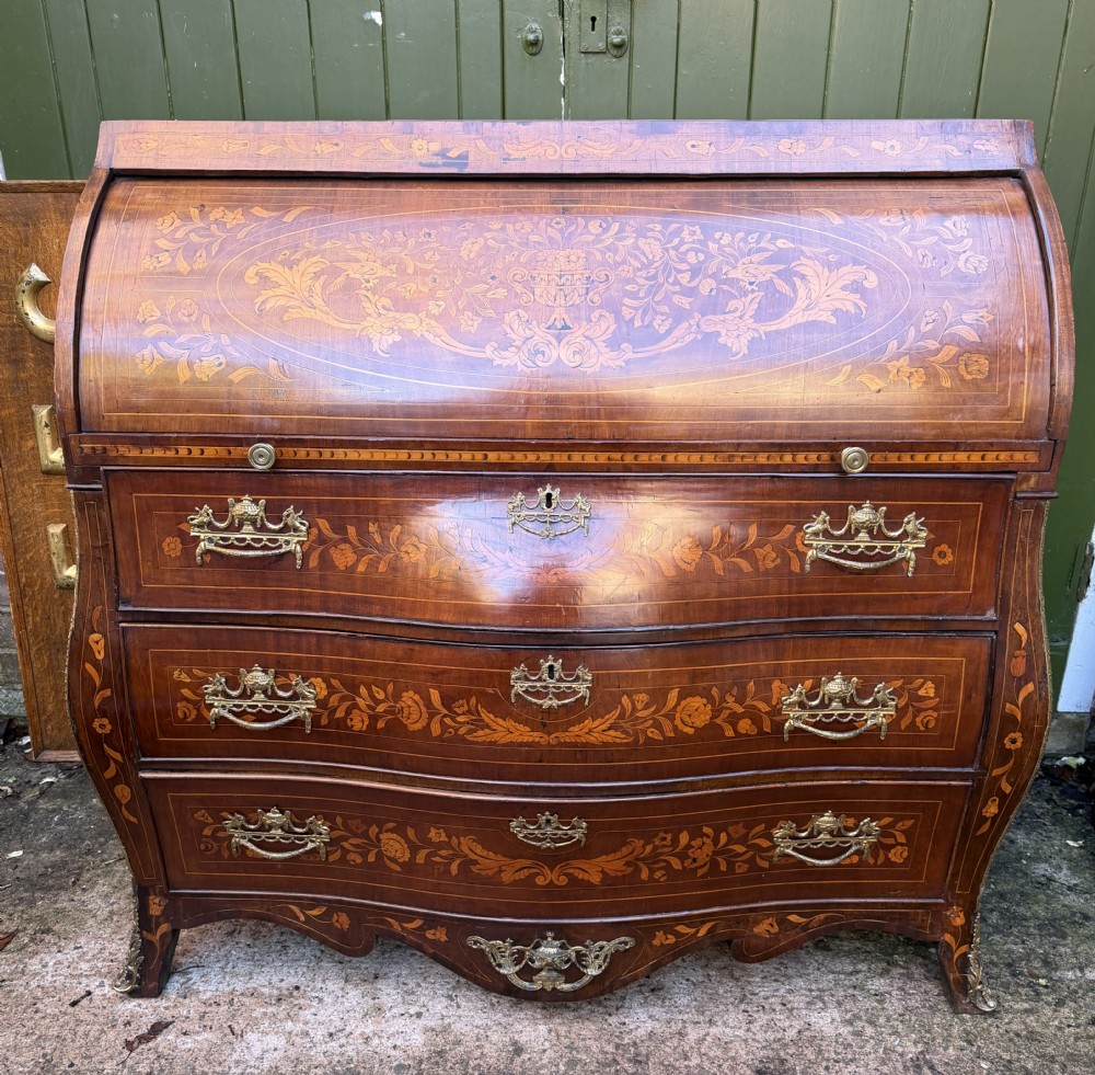 An antique Dutch walnut bureau with floral marquetry inlays, a curved cylinder front, three drawers, and decorative brass handles.