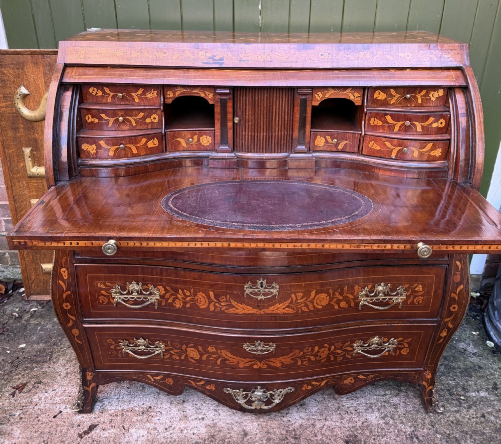 An antique Dutch walnut bureau with floral marquetry inlays, a curved cylinder front, three drawers, and decorative brass handles. View II