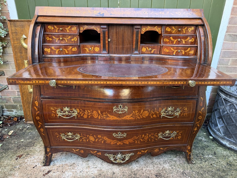 An antique Dutch walnut bureau with floral marquetry inlays, a curved cylinder front, three drawers, and decorative brass handles. View XIX