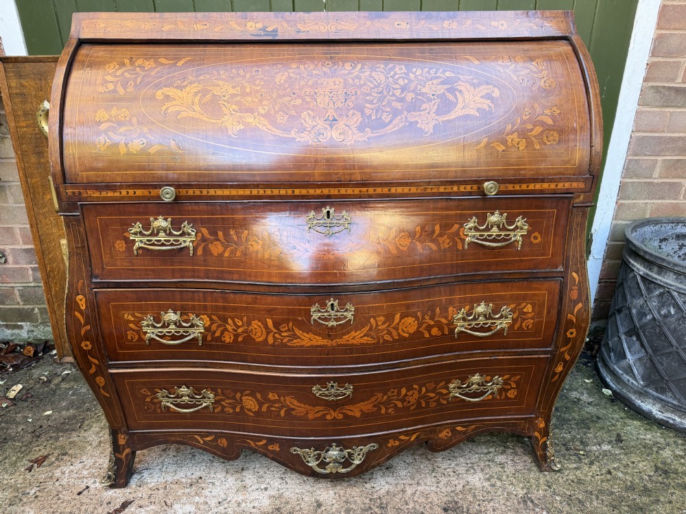 An antique Dutch walnut bureau with floral marquetry inlays, a curved cylinder front, three drawers, and decorative brass handles. View XXI