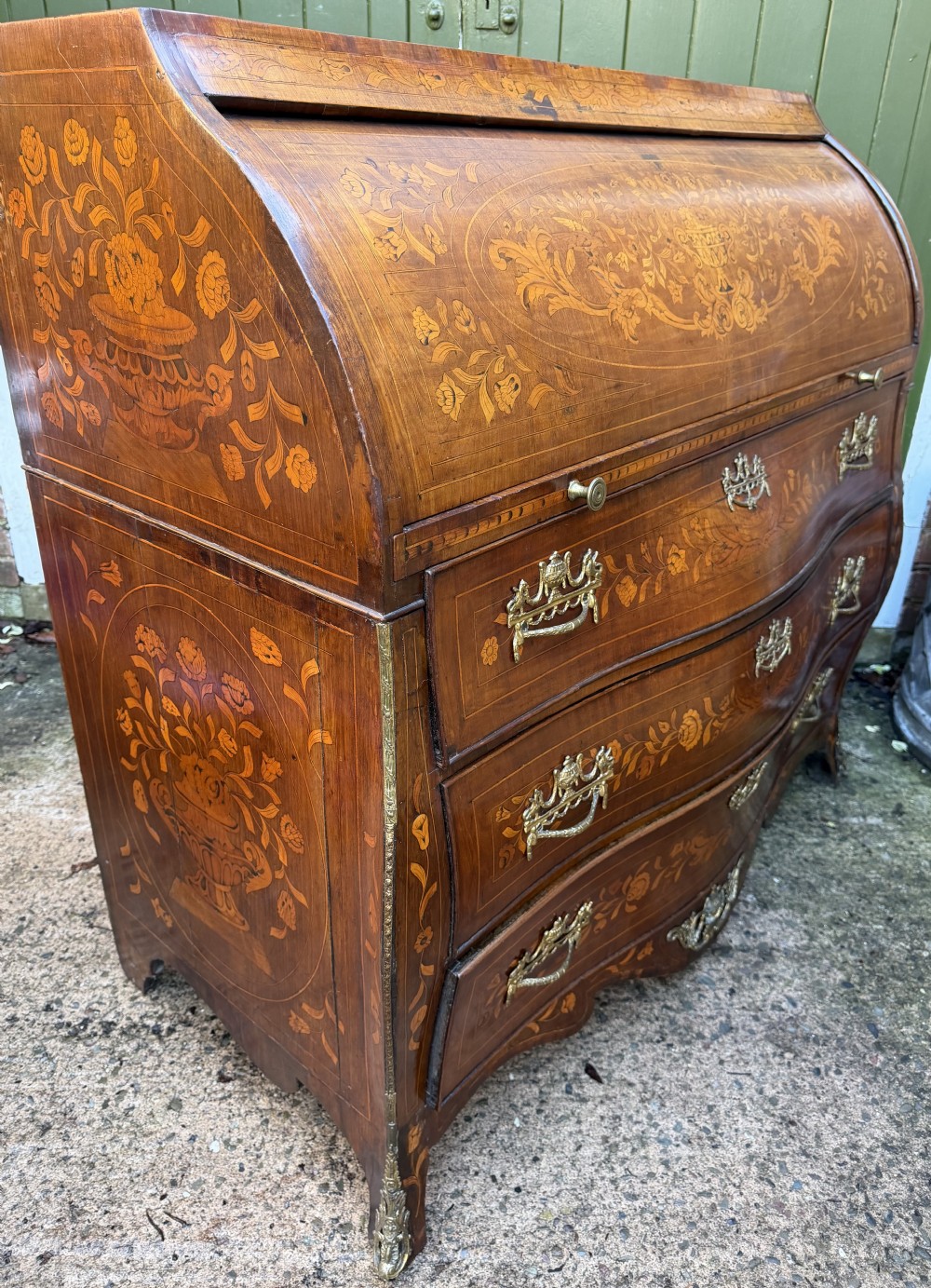 An antique Dutch walnut bureau with floral marquetry inlays, a curved cylinder front, three drawers, and decorative brass handles. View XXII