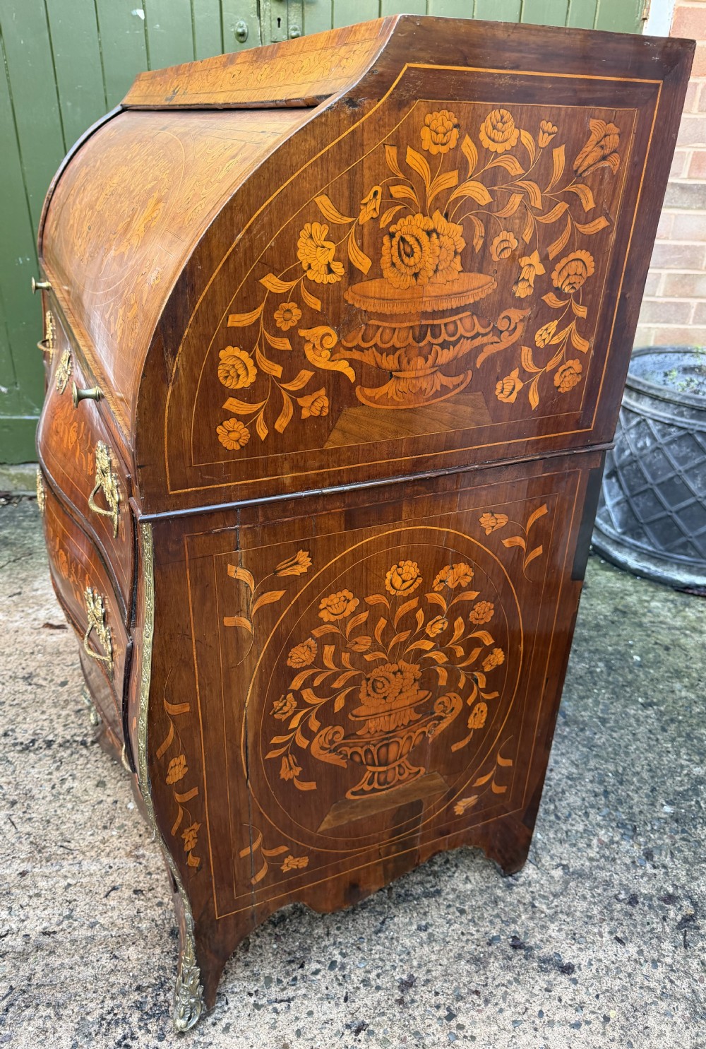 An antique Dutch walnut bureau with floral marquetry inlays, a curved cylinder front, three drawers, and decorative brass handles. View XXIV
