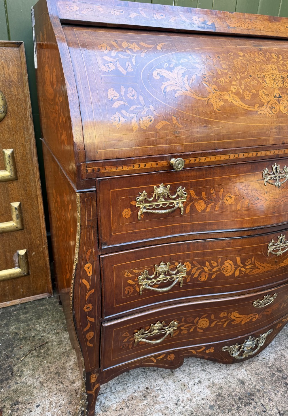 An antique Dutch walnut bureau with floral marquetry inlays, a curved cylinder front, three drawers, and decorative brass handles. View XXVI