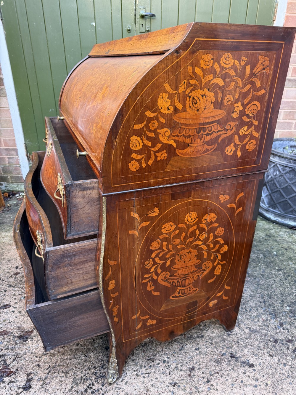An antique Dutch walnut bureau with floral marquetry inlays, a curved cylinder front, three drawers, and decorative brass handles. View XXVII
