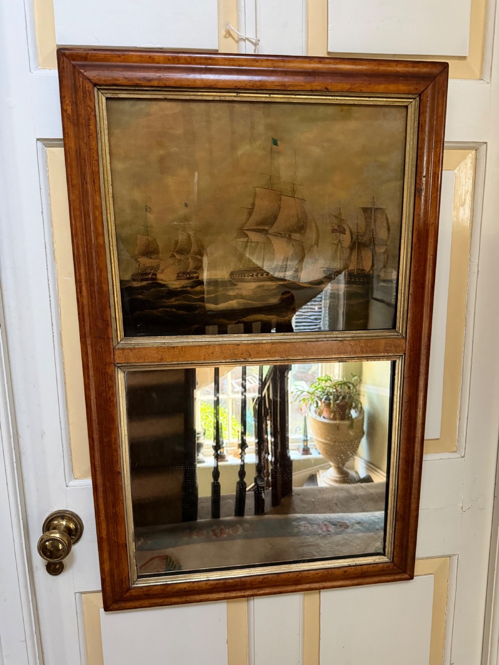 An early nineteenth-century rectangular maple-framed divided mirror featuring a reverse glass print of a naval engagement in the upper section and a reflective mirror below.