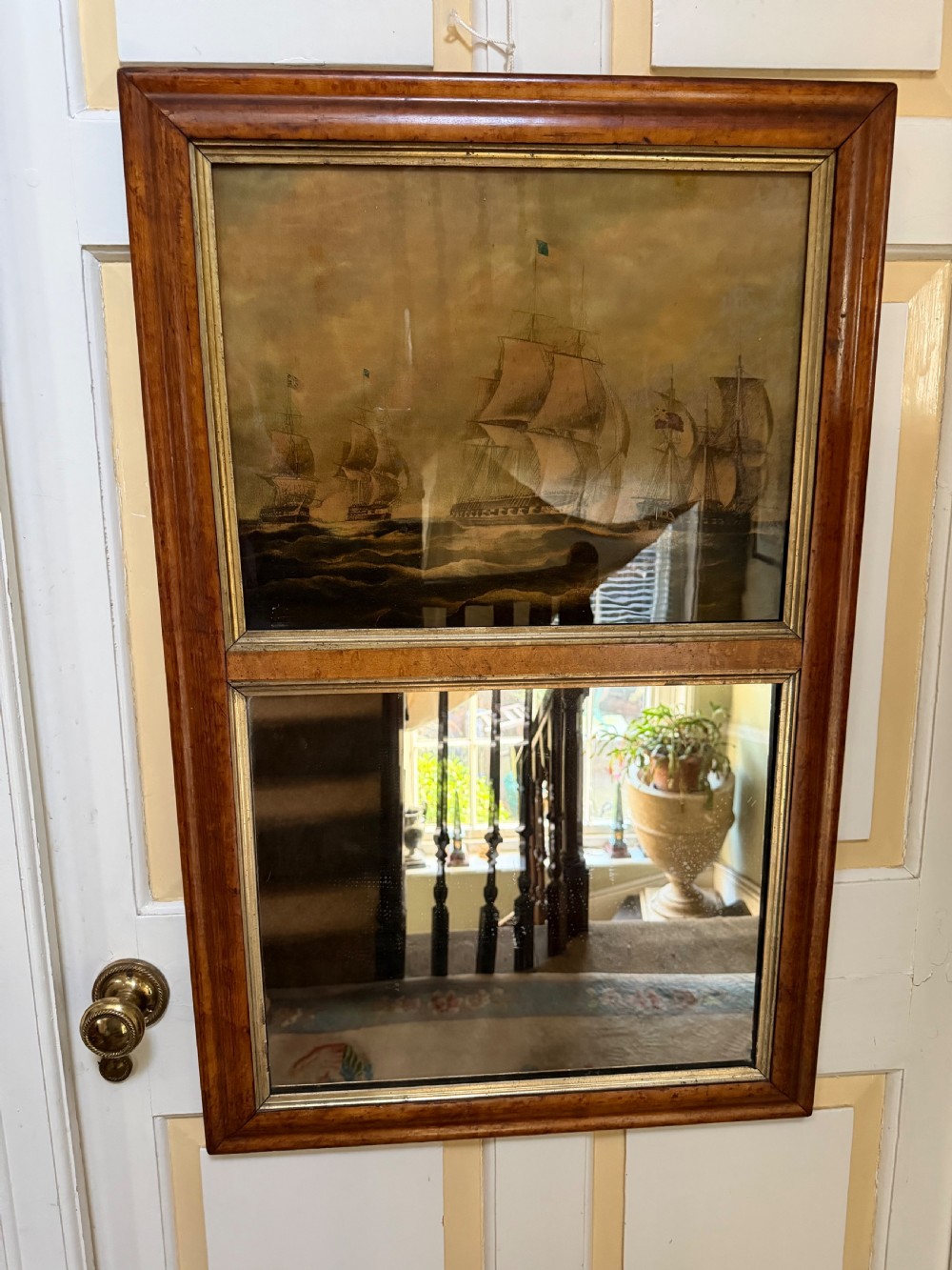 An early nineteenth-century rectangular maple-framed divided mirror featuring a reverse glass print of a naval engagement in the upper section and a reflective mirror below. View II
