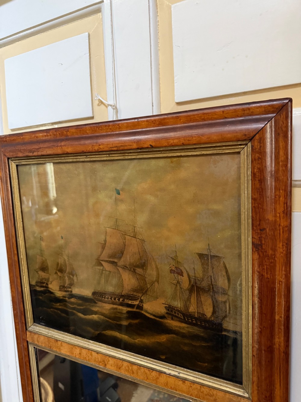 An early nineteenth-century rectangular maple-framed divided mirror featuring a reverse glass print of a naval engagement in the upper section and a reflective mirror below. View III