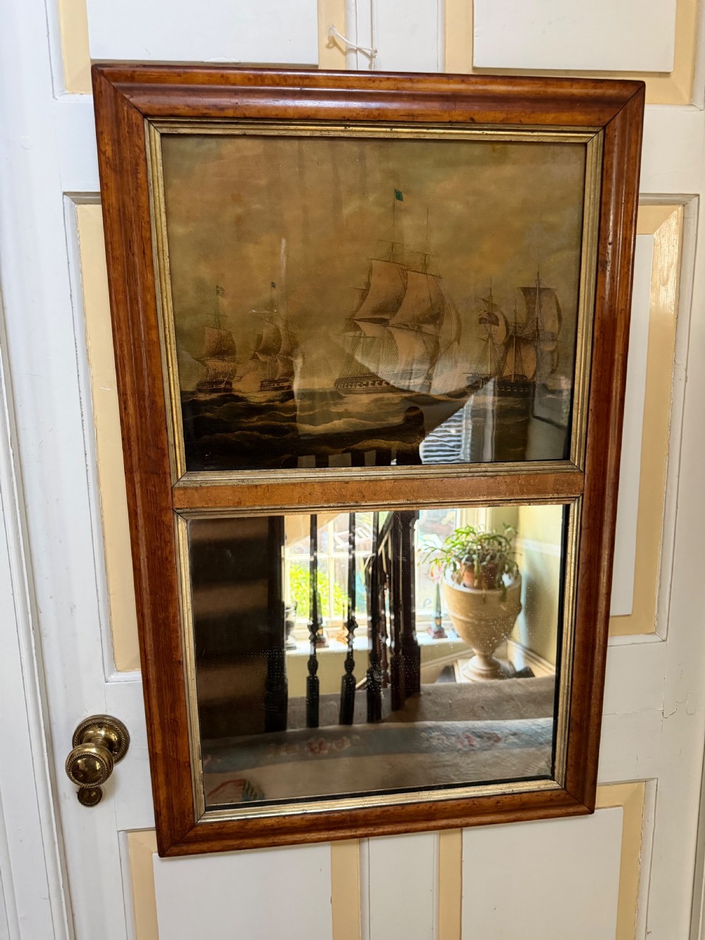 An early nineteenth-century rectangular maple-framed divided mirror featuring a reverse glass print of a naval engagement in the upper section and a reflective mirror below. View IV