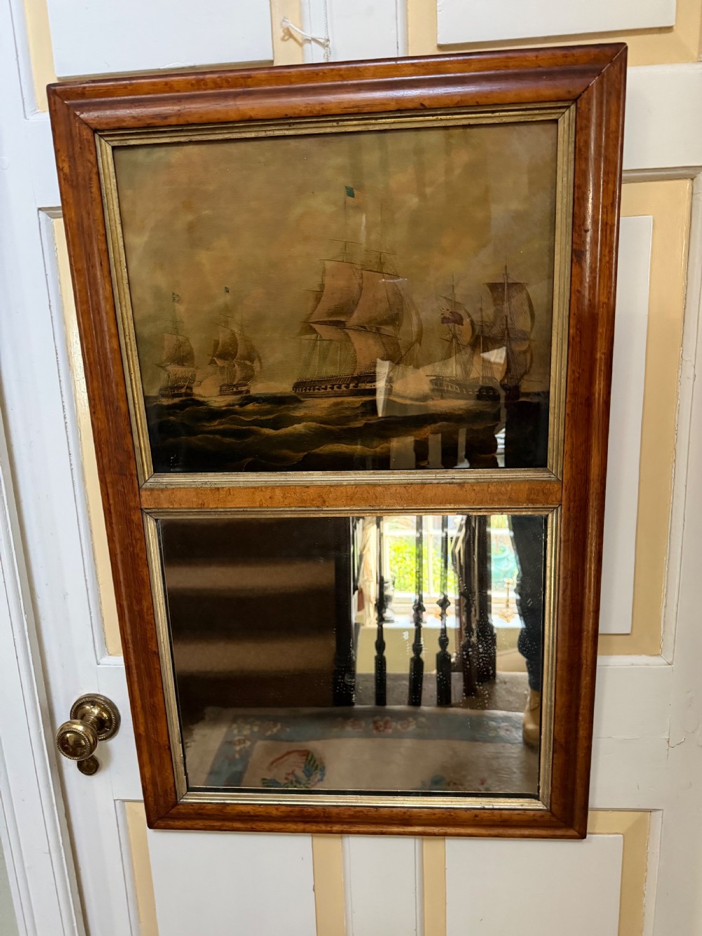 An early nineteenth-century rectangular maple-framed divided mirror featuring a reverse glass print of a naval engagement in the upper section and a reflective mirror below. View VI