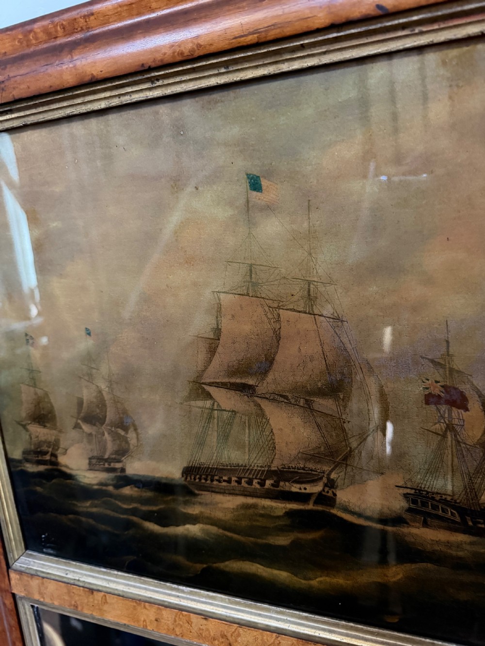 An early nineteenth-century rectangular maple-framed divided mirror featuring a reverse glass print of a naval engagement in the upper section and a reflective mirror below. View XI