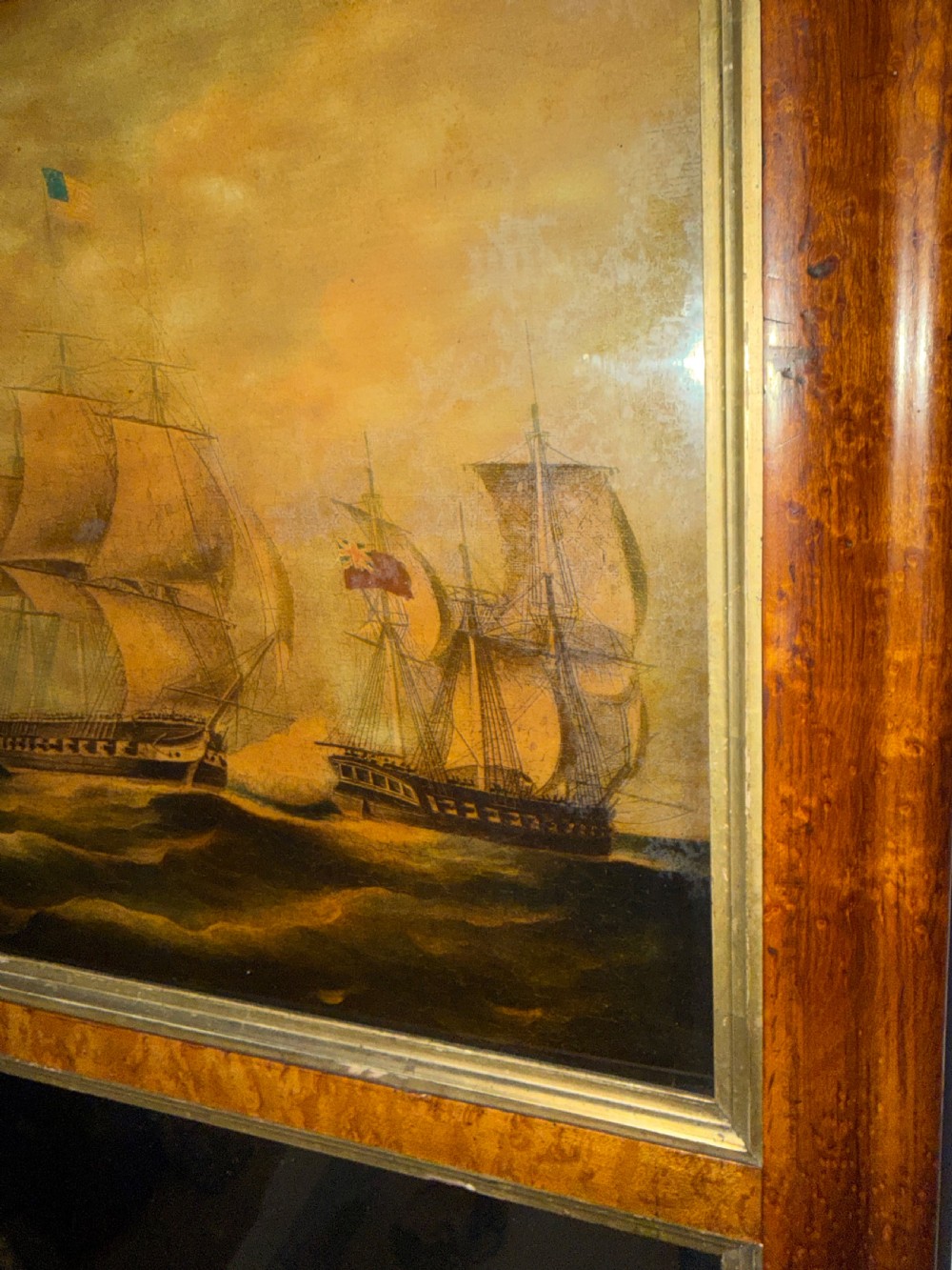 An early nineteenth-century rectangular maple-framed divided mirror featuring a reverse glass print of a naval engagement in the upper section and a reflective mirror below. View XII