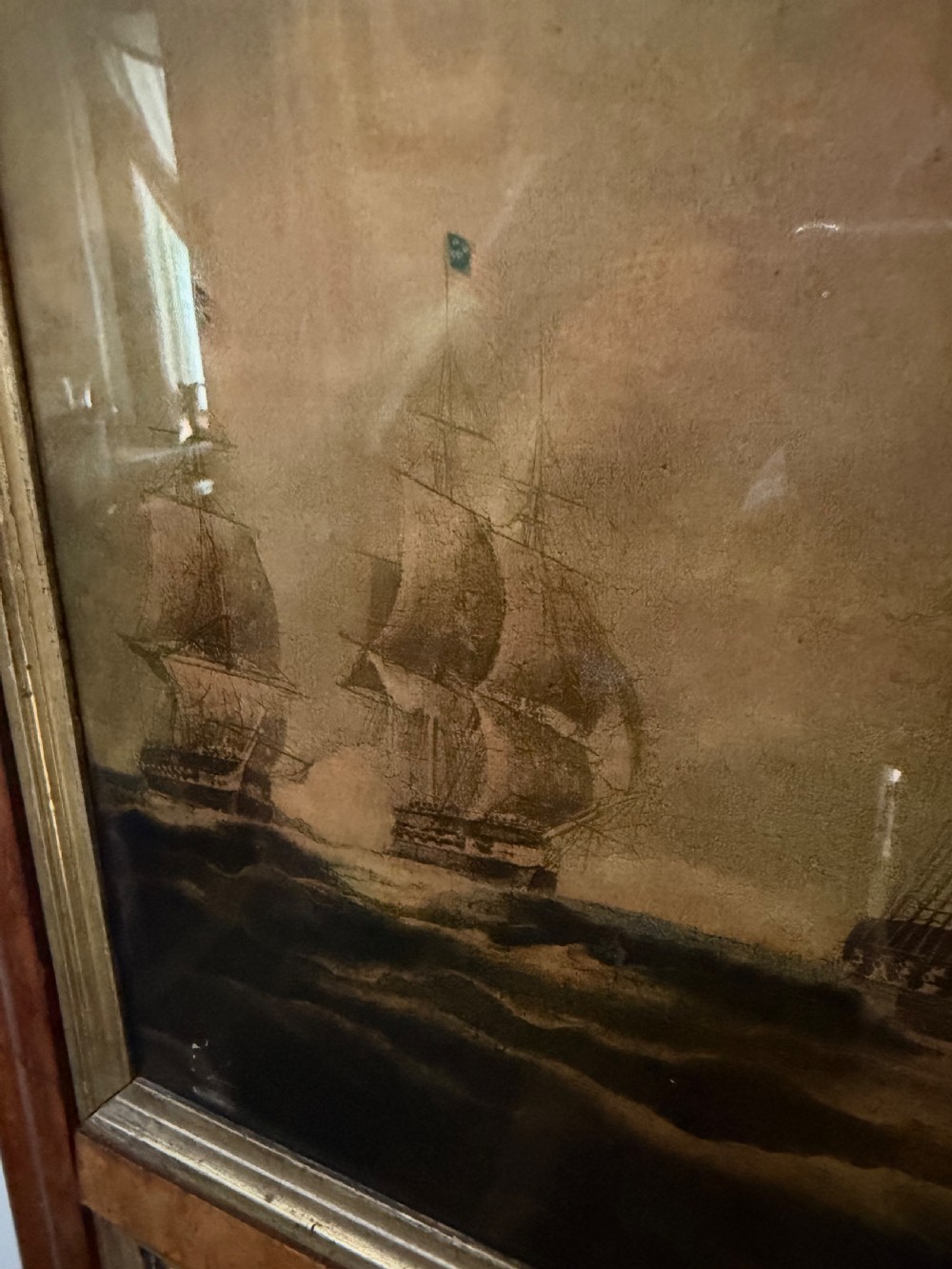 An early nineteenth-century rectangular maple-framed divided mirror featuring a reverse glass print of a naval engagement in the upper section and a reflective mirror below. View XIII
